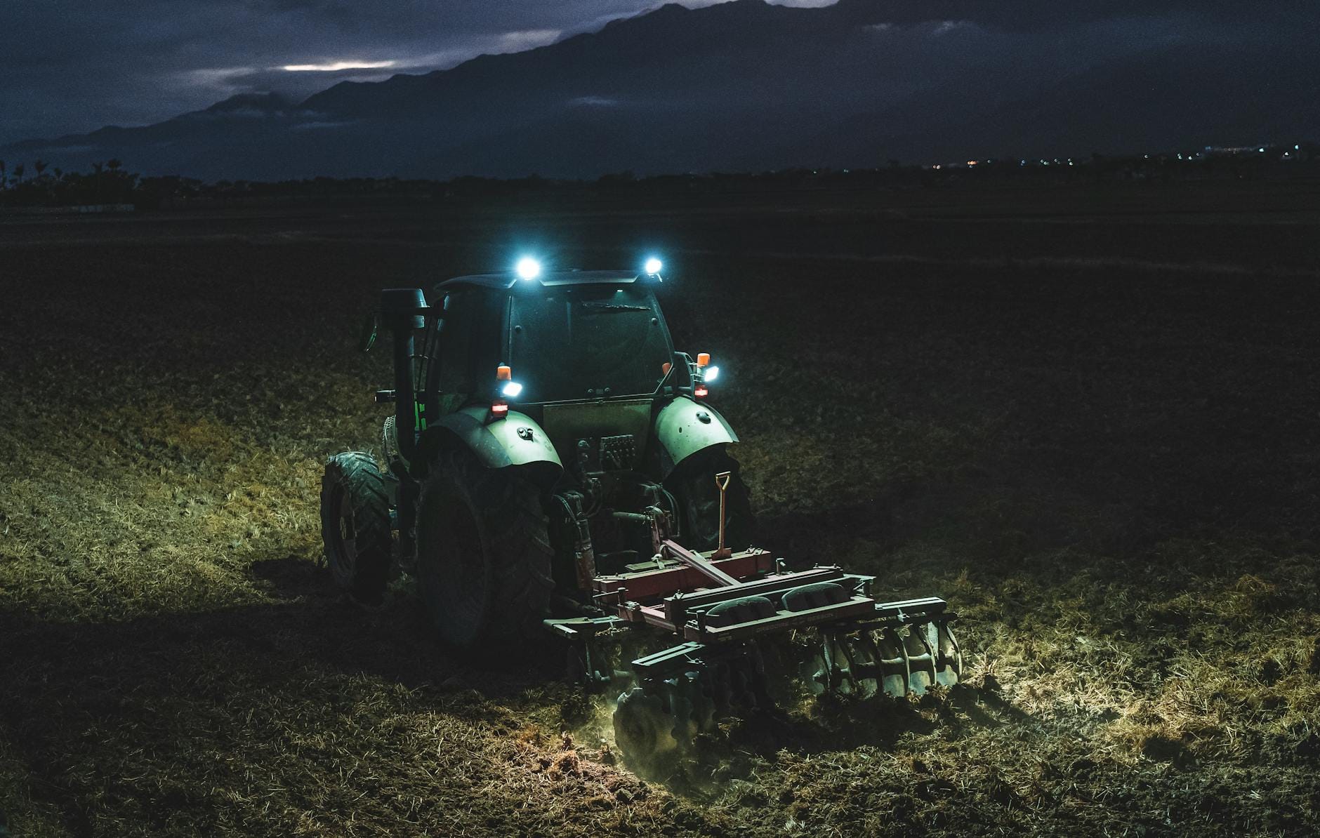 Ciągnik pracujący nocą na polu, oświetlony reflektorami