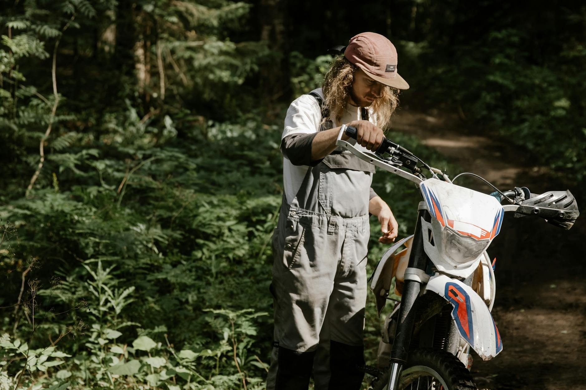 Mężczyzna w kombinezonie przy motocyklu w gęstym lesie