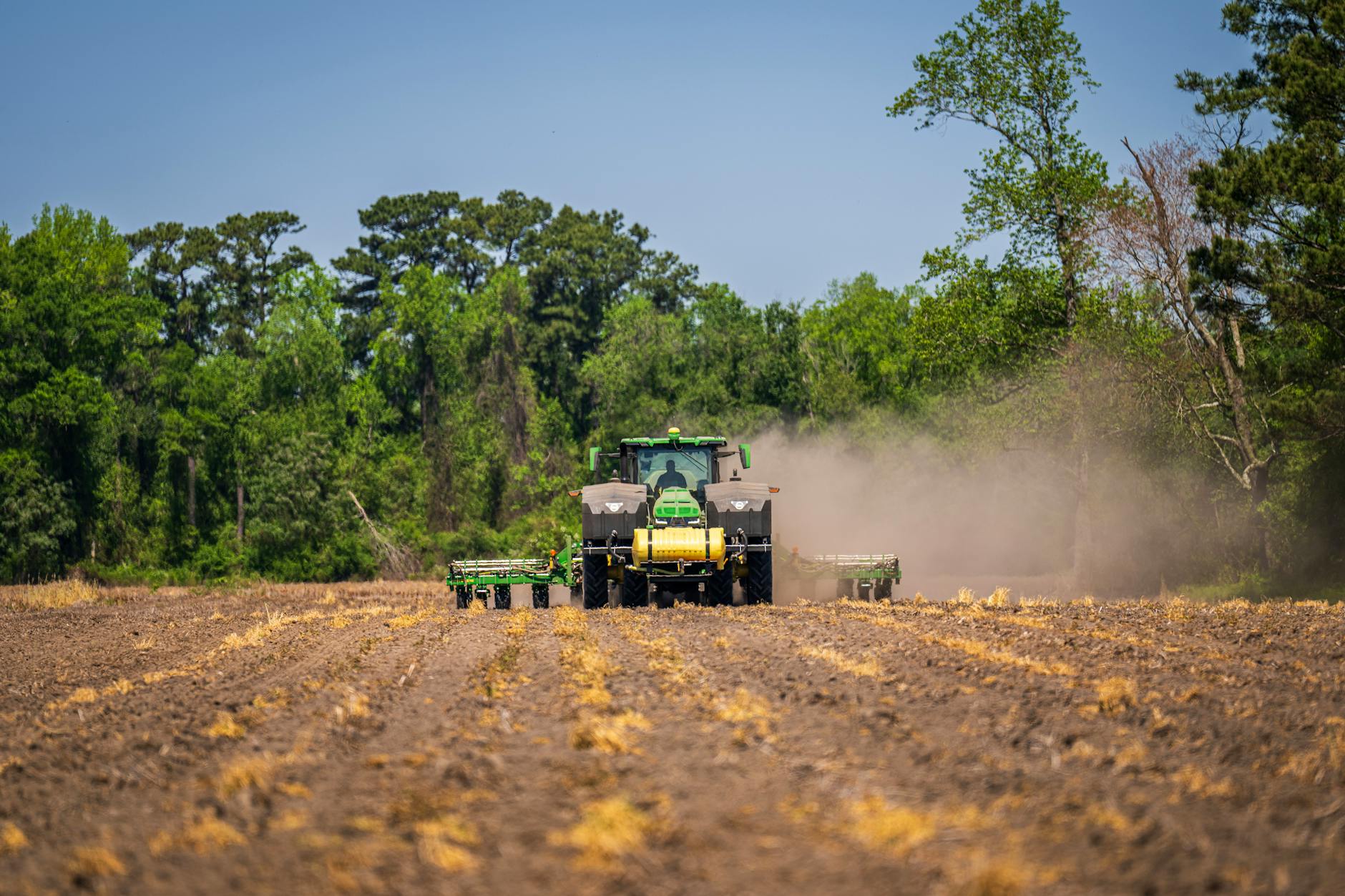 Ciągnik orze zapylone pole w otoczeniu zielonych drzew na wsi