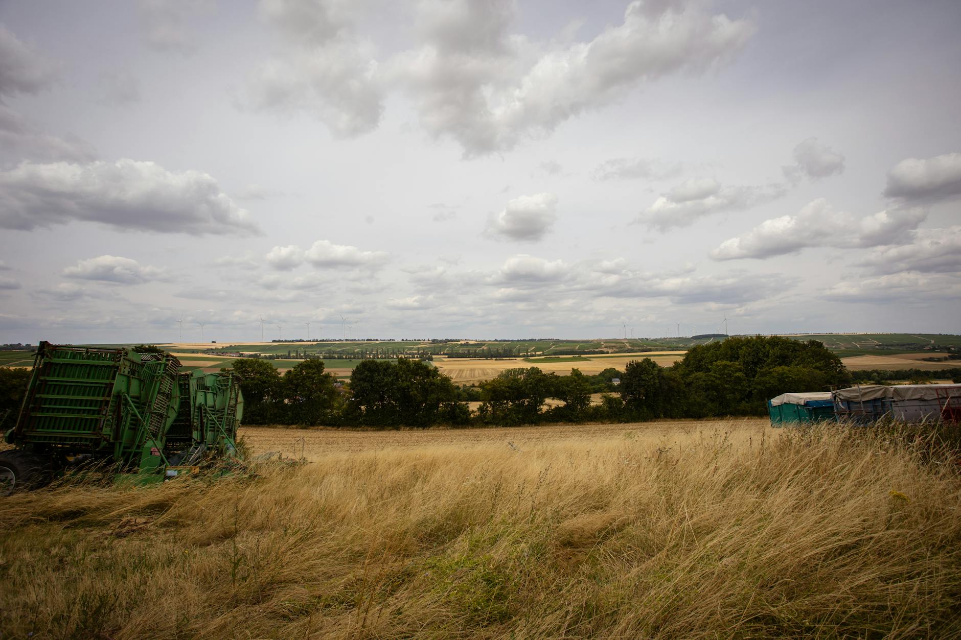 Maszyny rolnicze pracujące na rozległym polu pod pochmurnym niebem