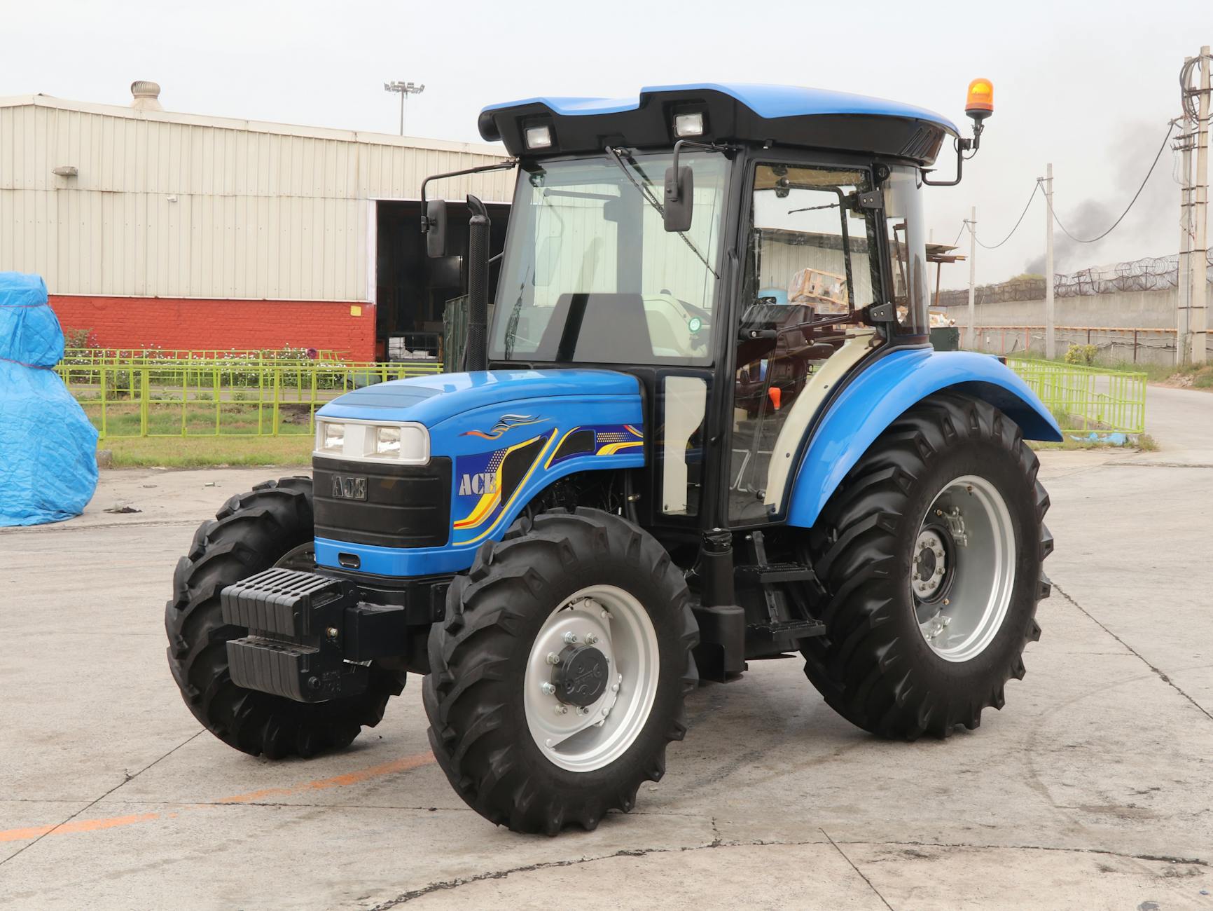 Nowoczesny niebieski traktor 4x4 na tle zabudowań przemysłowych Nowoczesny niebieski traktor 4x4 na tle zabudowań przemysłowych