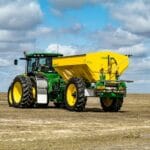 Zielony ciągnik Ursus z przyczepą na polu pod błękitnym niebem