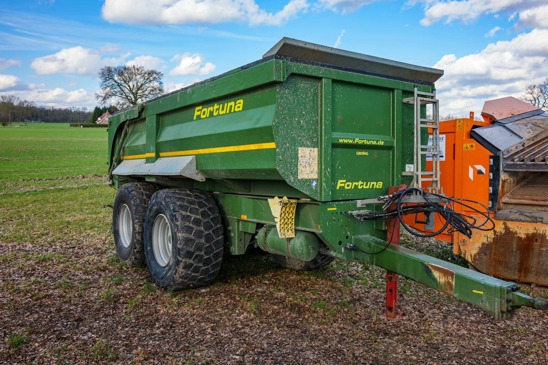 Przyczepy rolnicze: hamulce pneumatyczne czy hydrauliczne? Zielona przyczepa rolnicza Fortuna zaparkowana na polu w Niemczech