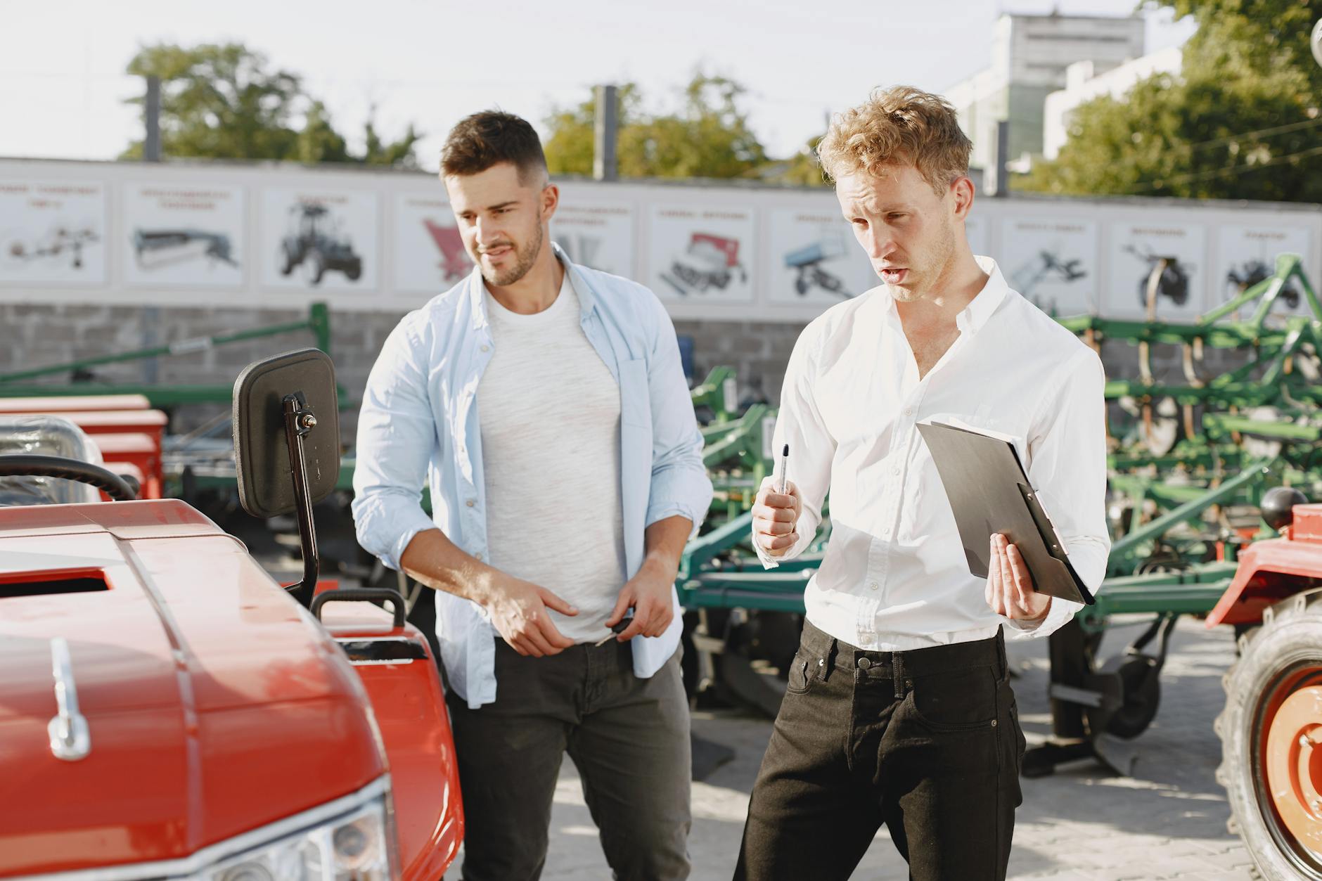 Dwóch rolników rozmawia o sprzedaży ciągnika na placu maszyn