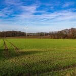 Zielone pola uprawne z turbiną wiatrową na tle błękitnego nieba